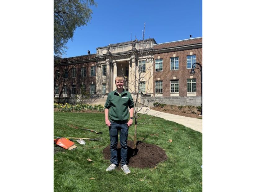 Gavin Maxson stands with a tree he just planted in front of the Henderson Building