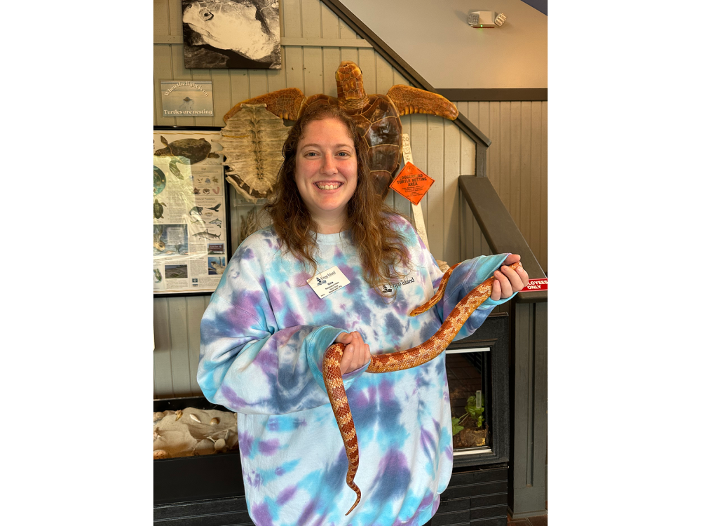 A woman holds a small orange snake in a room.