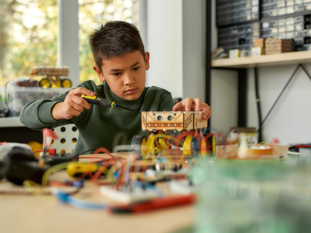 Boy using screwdriver while fixing bolts on a robot vehicle. Smart kids and STEM education.