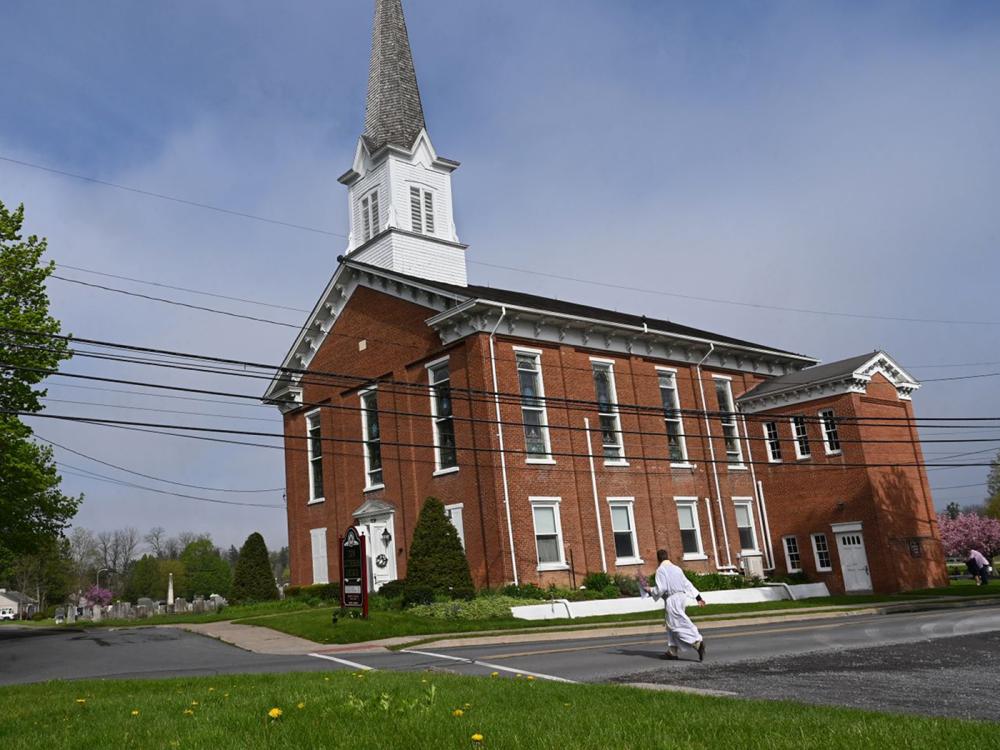 Man in white robe walks toward a red brick church