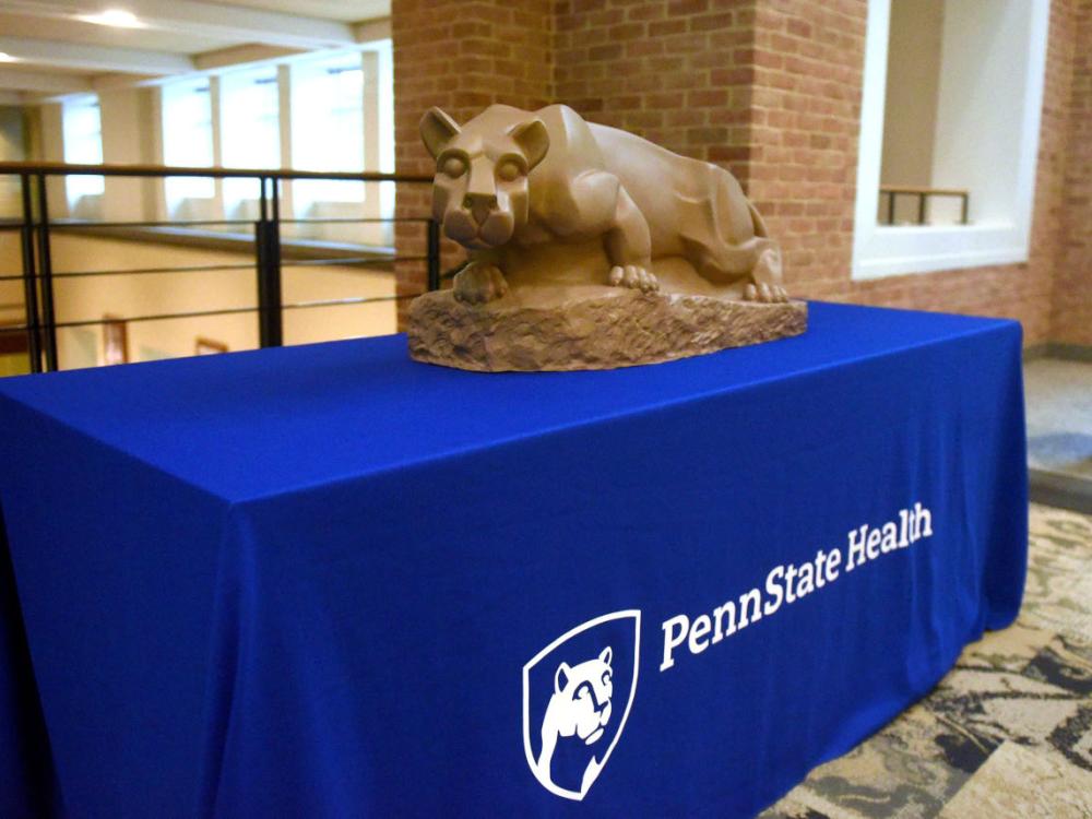 A Nittany Lion statue sits atop a table draped with a “Penn State Health” tablecloth.