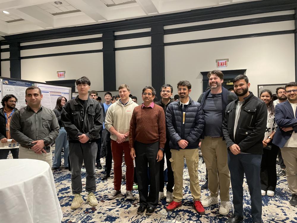 Penn State students and faculty stand in a line for a photo surrounded by their research posters during poster session.