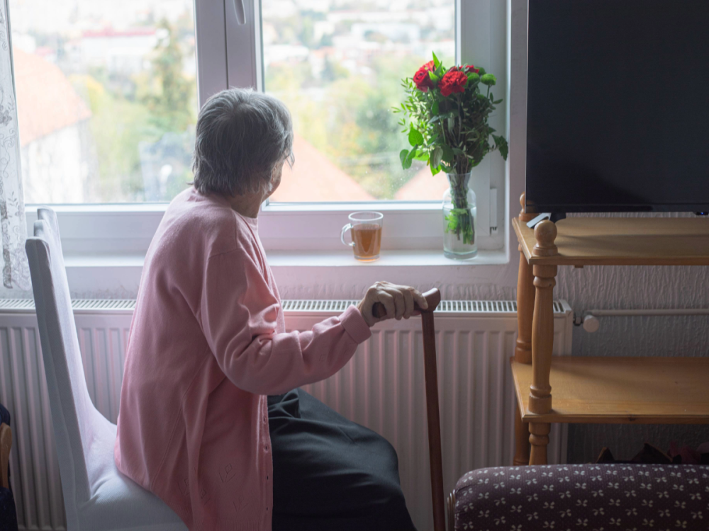 A senior woman holding a cane, looking out a window