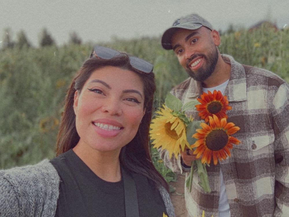a woman and man holding sunflowers pose for a photo in a sunflower field