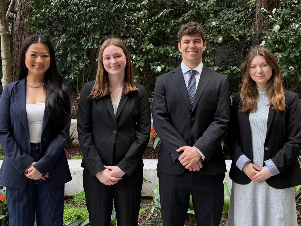 A photo of four people wearing business attire and posing outside.