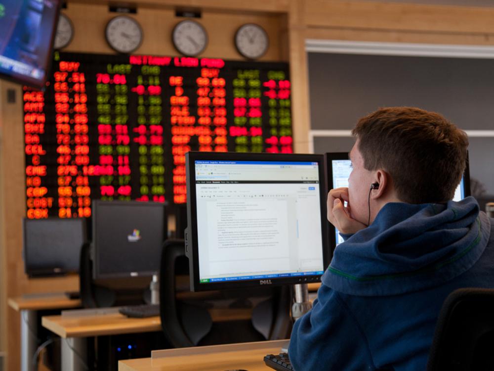 A photo of a student from behind looking at a computer monitor in the Rodgers Family Trading Room in the Business Building