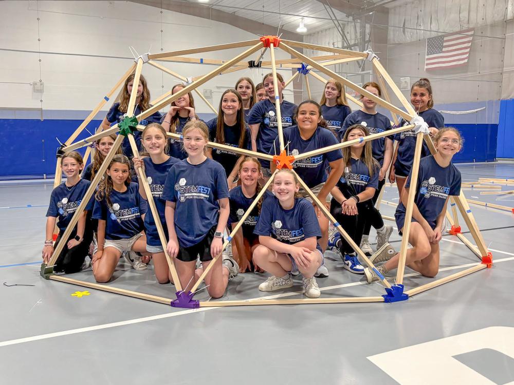 A group of students grouped together under a geodesic dome made of connectors