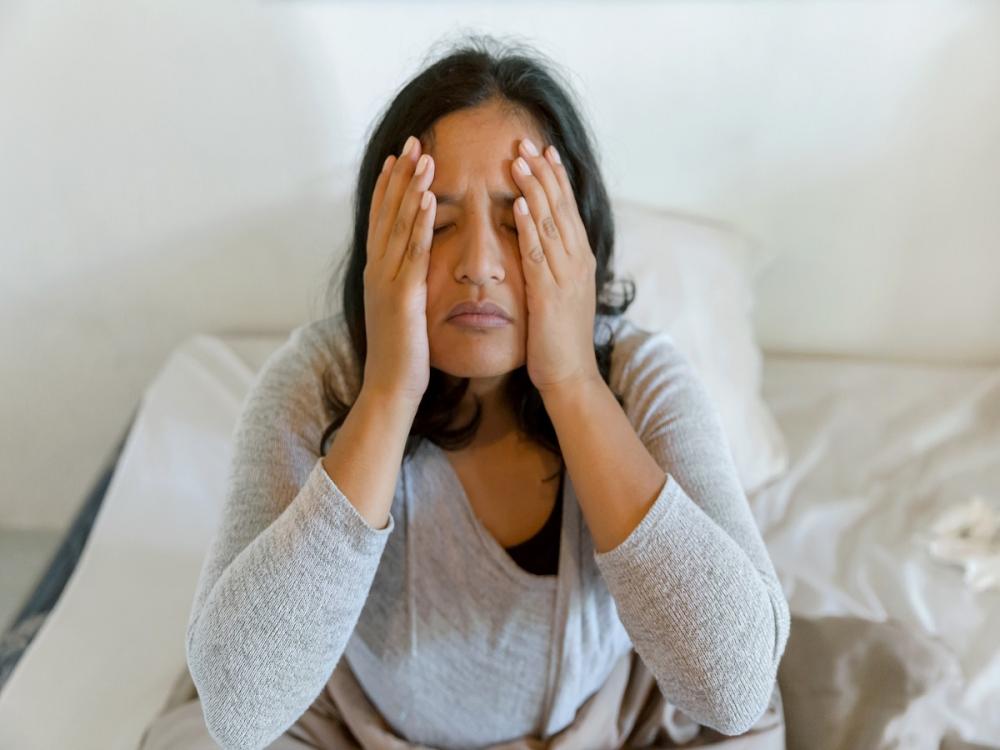 A woman rubs her head as she sits up in bed.
