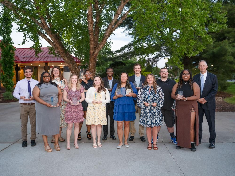 A group of smiling students stand together outside a restaurant