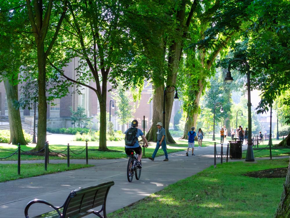 The sidewalk of Henderson building with a person biking and people walking. 
