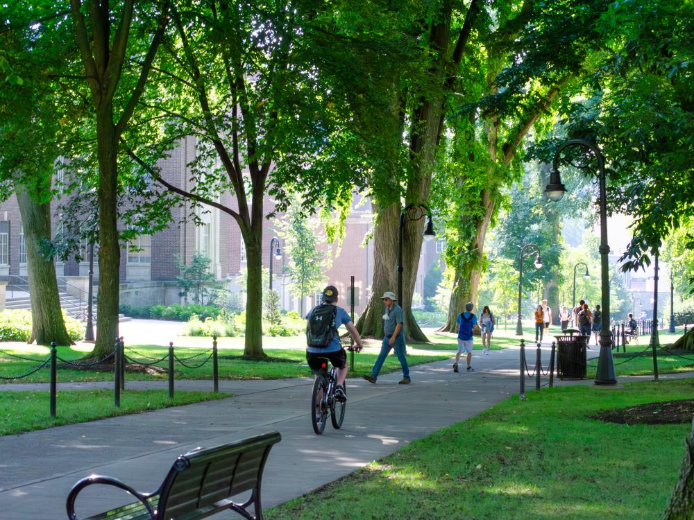 The sidewalk of Henderson building with a person biking and people walking. 