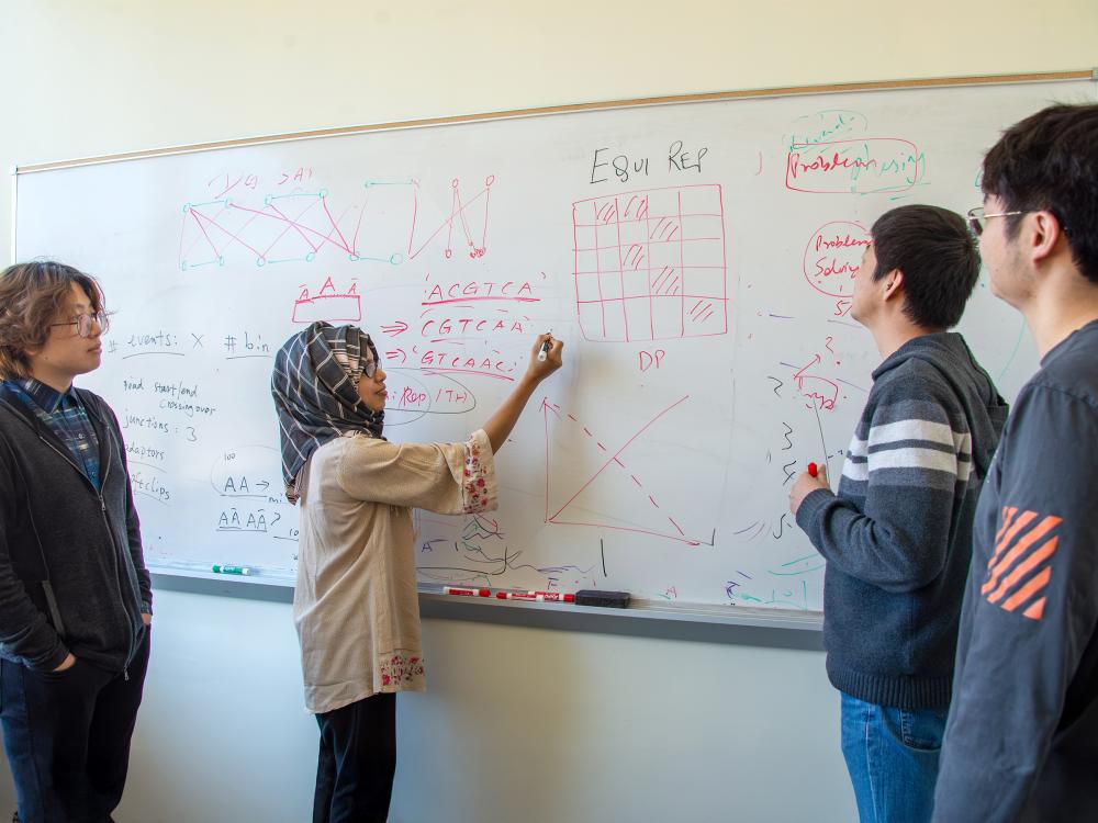Four people look at a whiteboard. 