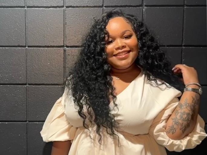 Iyana Burrows stands in a white dress smiling against a black wall.