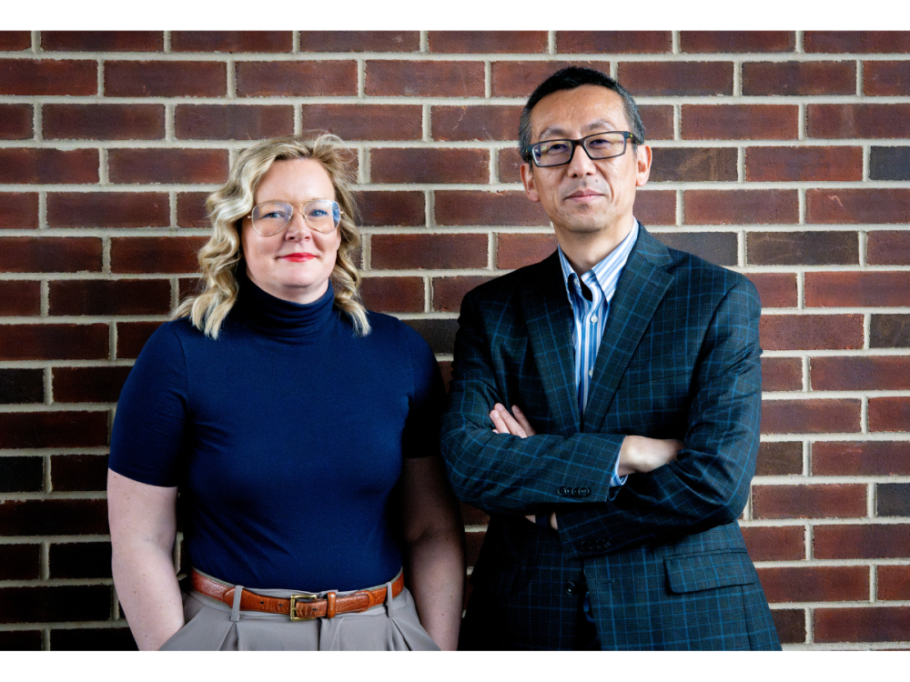 From left, Nikki Crowley and Nanyin Zhang pose for a photo in front of a red brick wall.