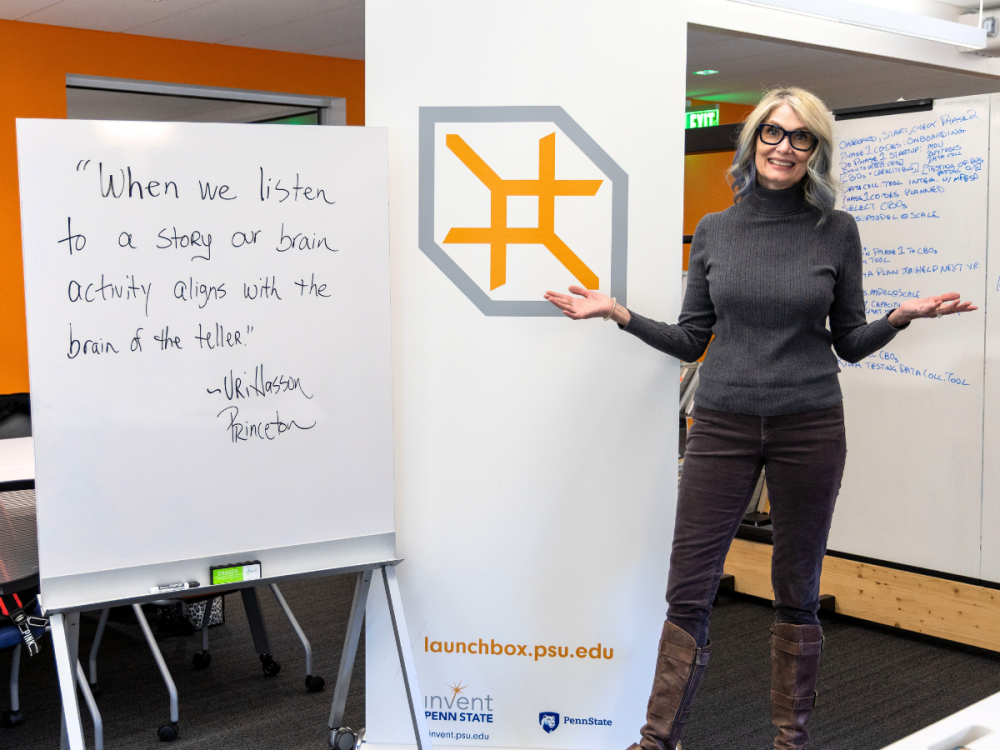 Dawn Ziegerer stands in front of a LaunchBox banner and a white board that says "When we listen to a story our brain activity aligns with the brain of the teller." - Uri Hasson, Princeton