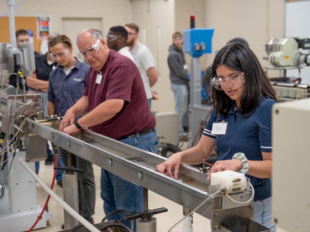 Several students work in a row at a machine that extrudes screws