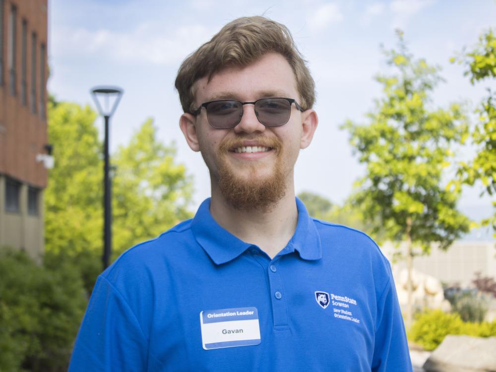 Student with glasses smiling with trees in the background