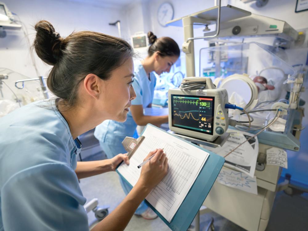 Two nurses monitor a baby in a neonatal intensive care unit