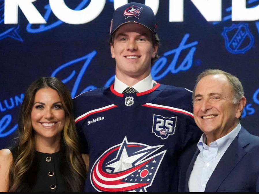 Jackson Smith wears a Columbus Blue Jackets hat and jersey flanked by Meredith Gaudrea and Gary Bettman. 