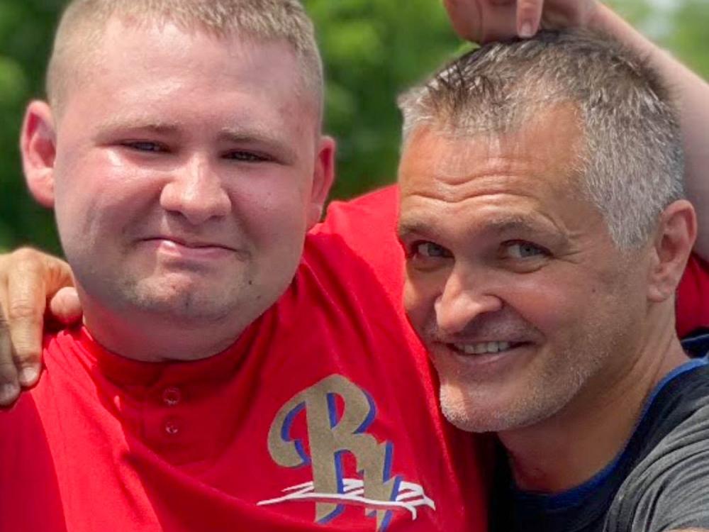 Two people, father and son, smile and point at the camera