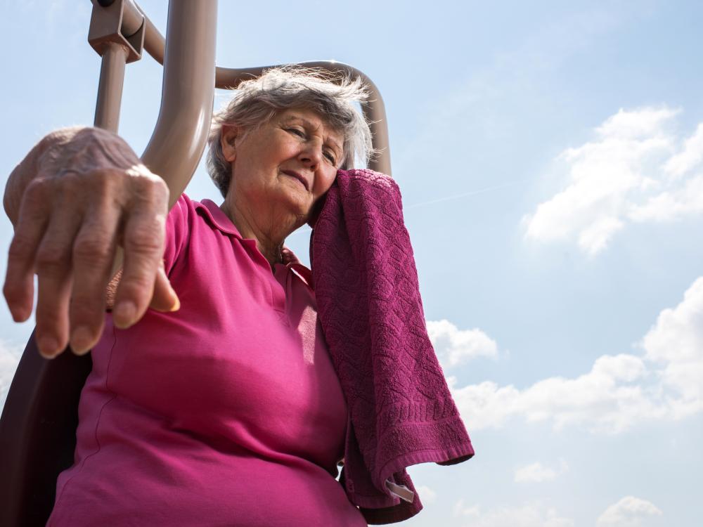 An older woman leans mops her brow in the sunshine