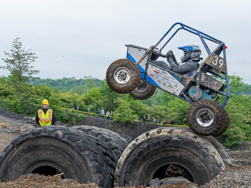 An all terrain vehicle drives over huge tires while a person watches