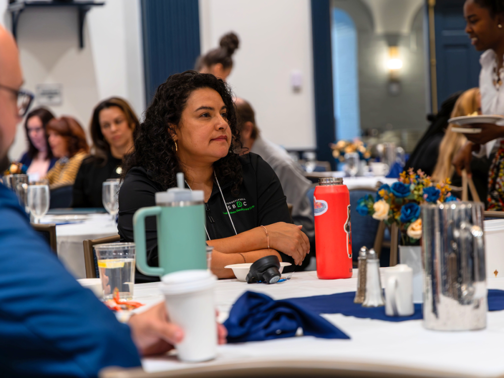 Individual wearing an SBDC jacket sits at a table at a conference setting