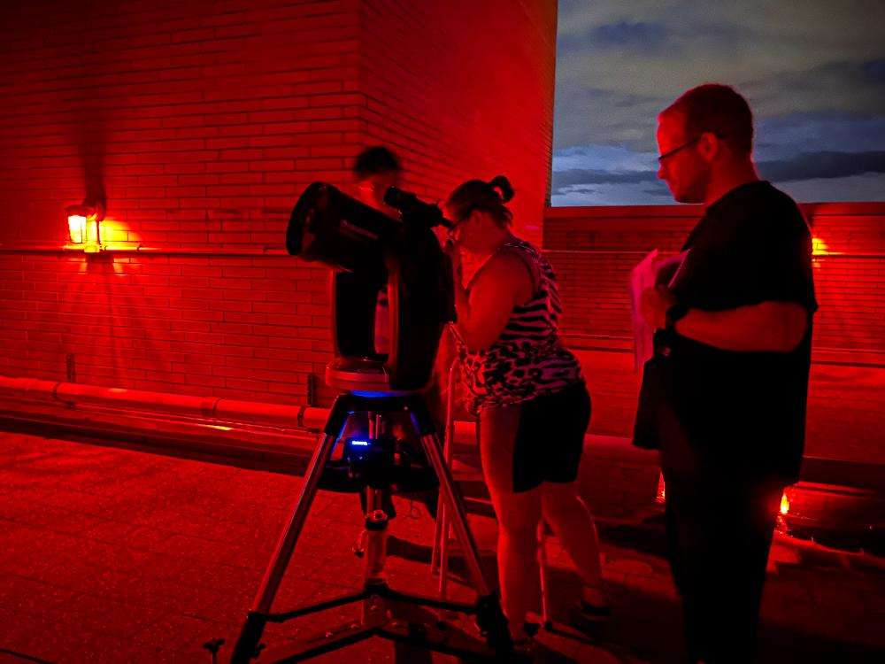 A person looking through a telescope with two people standing next to her.