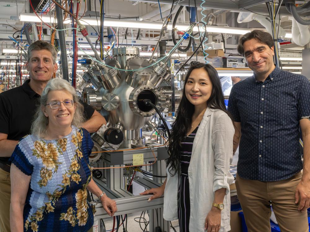 Four people stand in front of machinery in a lab