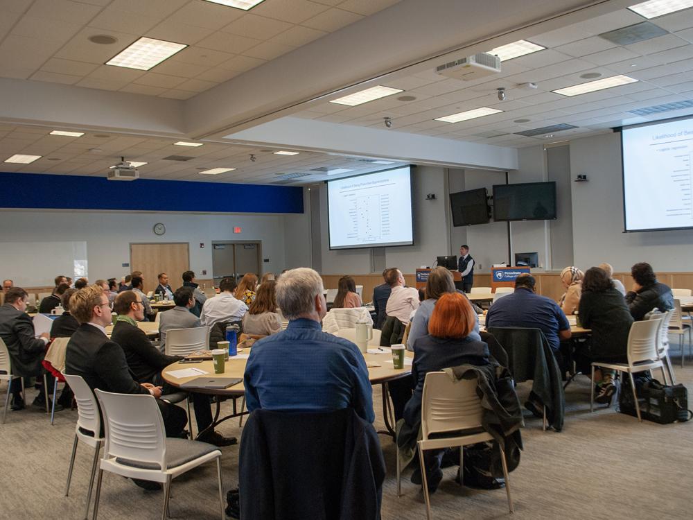 A group of people at tables watch a presentation on big screens