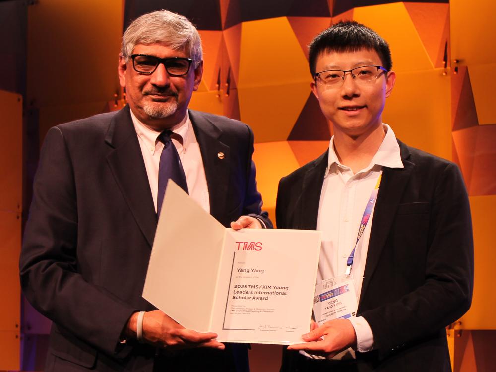 Two people looking at the camera and holding an award