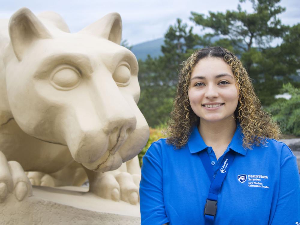 Student smiles for a picture, sitting next to Penn State Scranton's lion shrine. 