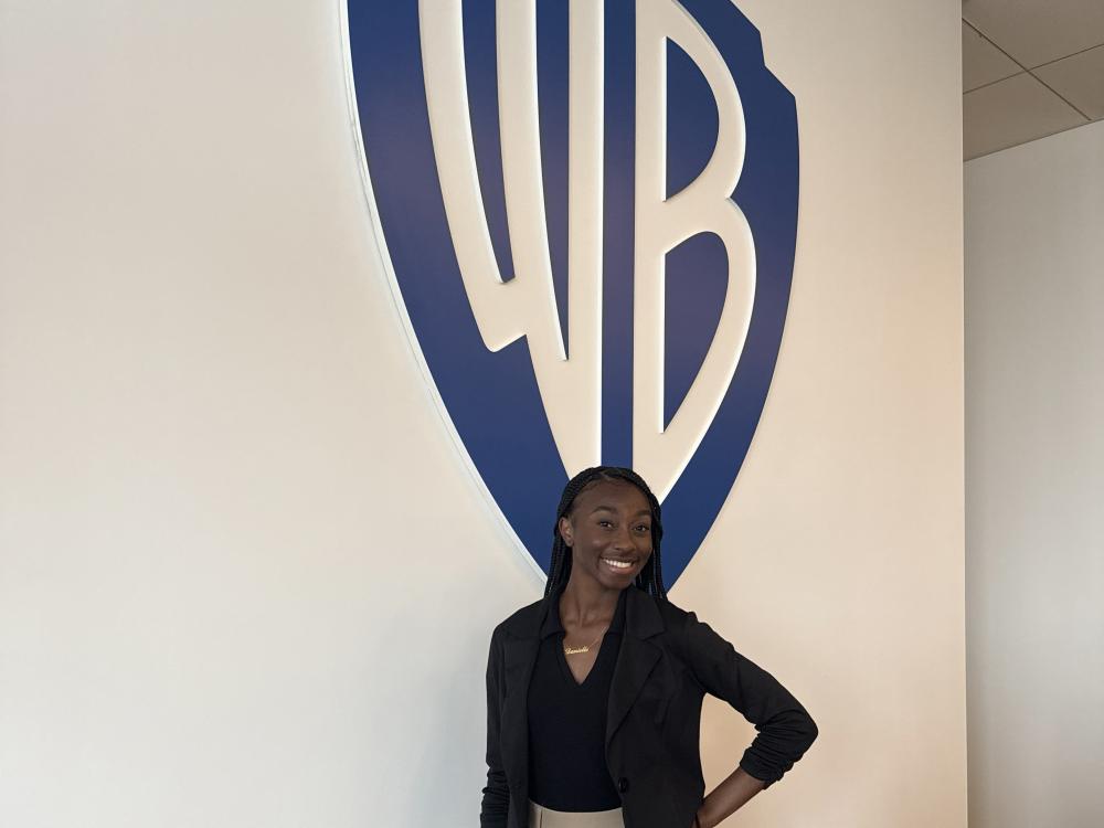 Danielle Sanois stands in front of the Warner Bros. logo.