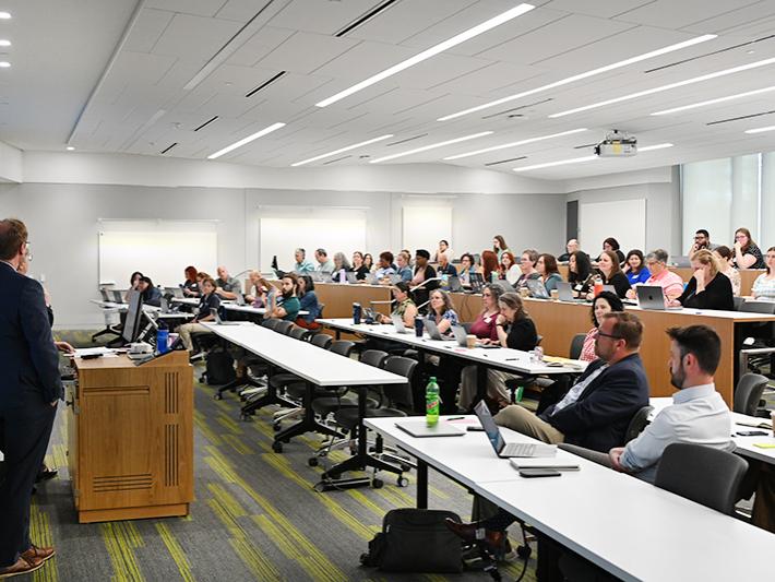 A crowd sits in a large lecture hall listening to a speaker.
