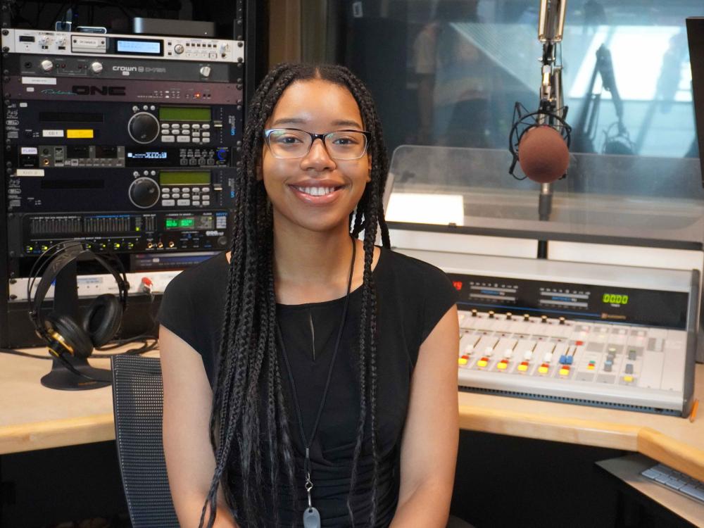 College student smiling as she is sitting in a sound booth at a radio station.