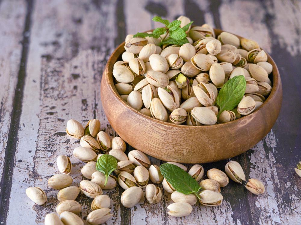 A small wooden bowl overflowing with pistachios and topped with sprigs of mint