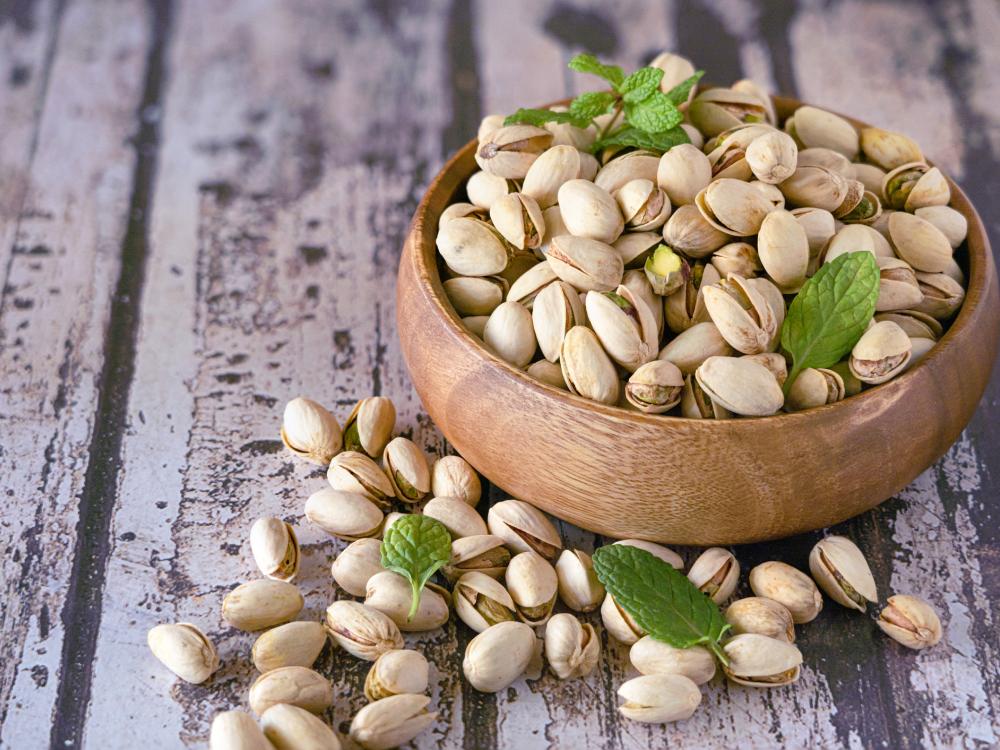 A small wooden bowl overflowing with pistachios and topped with sprigs of mint