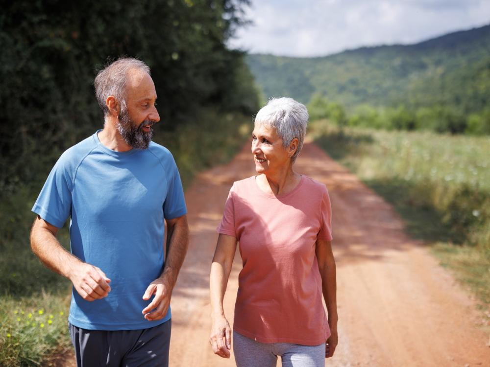 Mature couple walks together in nature on sunny day.