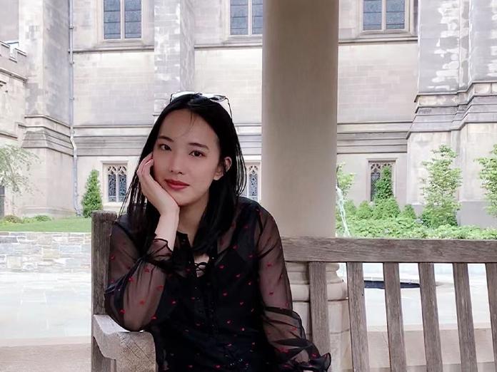Person with dark hair sitting on a bench smiling
