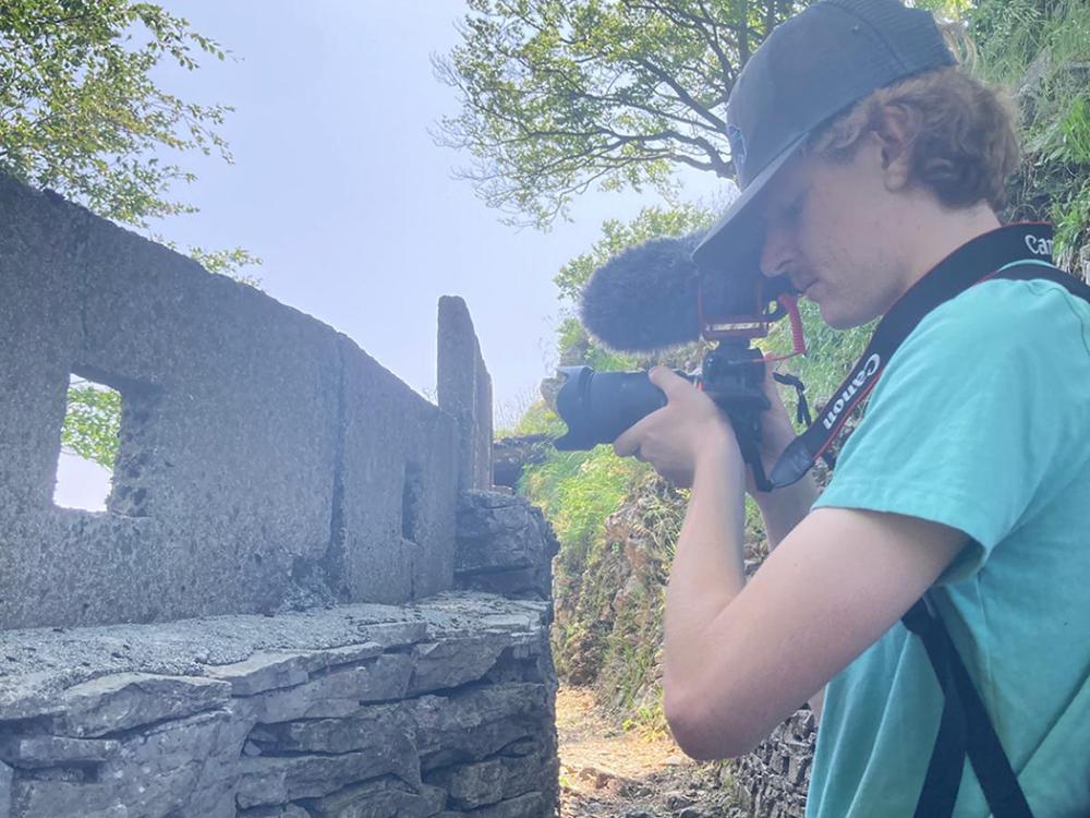 A student in a ballcap holds a camera and focuses on a shot