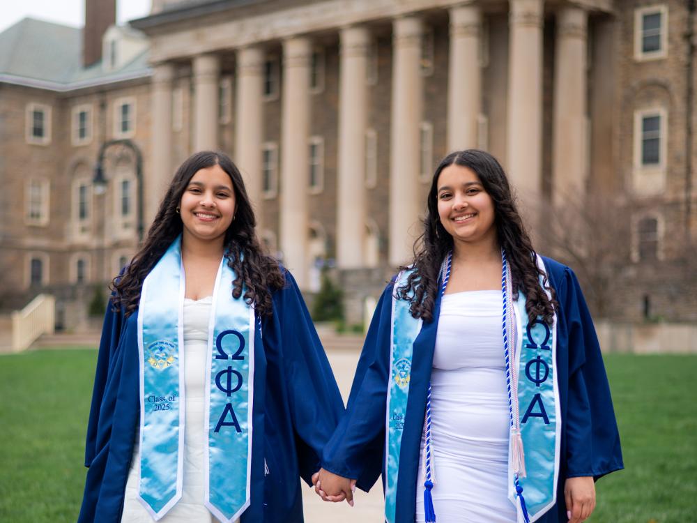 Olivia (left) and Abby Kayani stand in graduation gowns outside Old Main.
