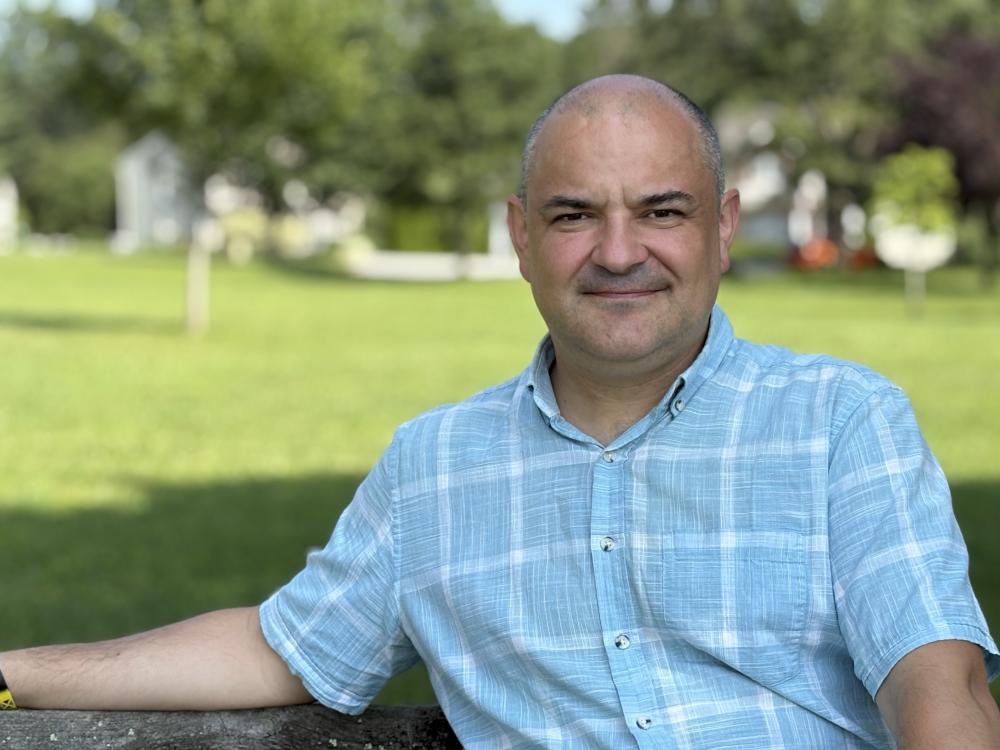 Martin Marinos sitting on a park bench with blue skies behind him.