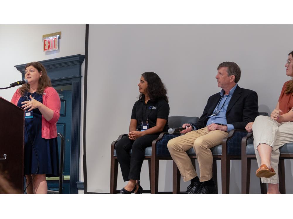 Group of three presenters sitting down for a panel discussion. To the left is Heather Robbins, who is moderating the panel.