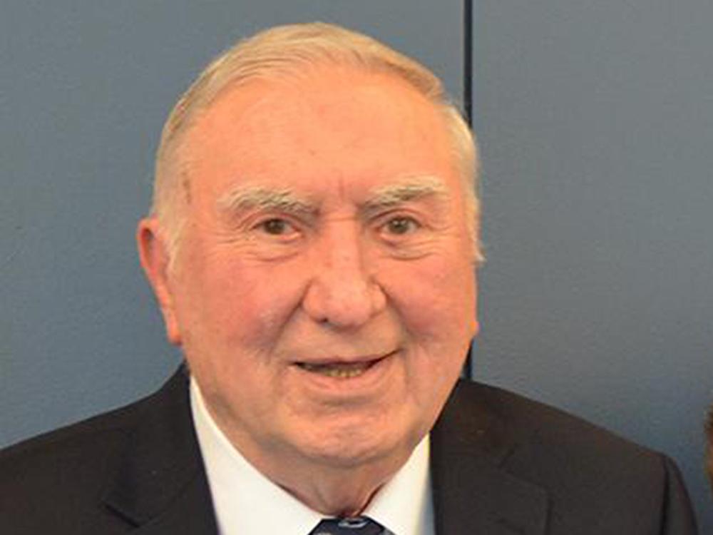 Smiling man with thinning gray hair wearing a coat and tie