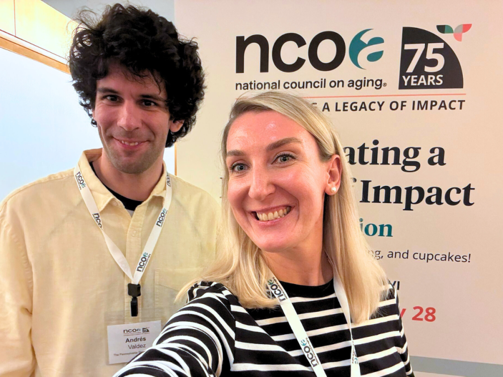 Two people stand in front of a stand-up banner in a conference setting