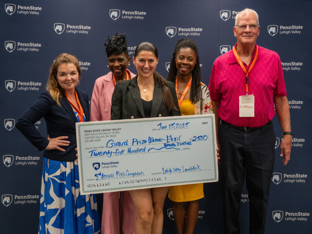 a woman, smiling holds a large check with people beside her