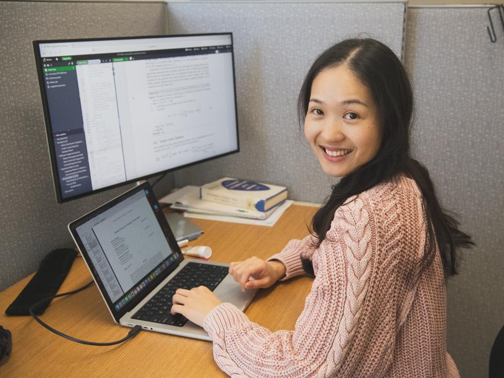 Postdoc Shurong Lin sitting at computer, looking at camera