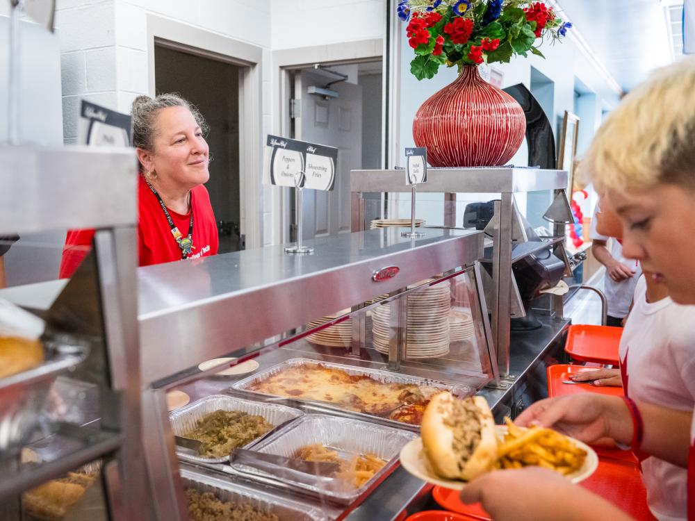 A student serves a team member food in a cafeteria