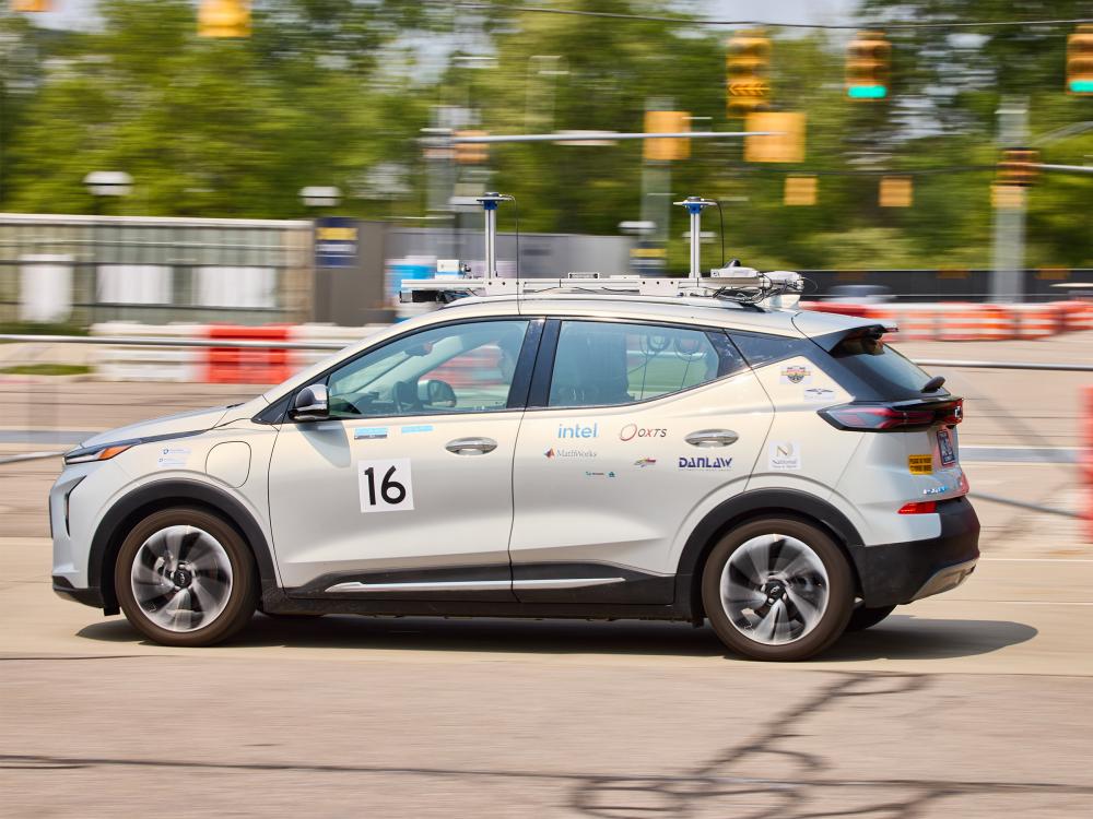 A silver sedan is seen moving across a race course.