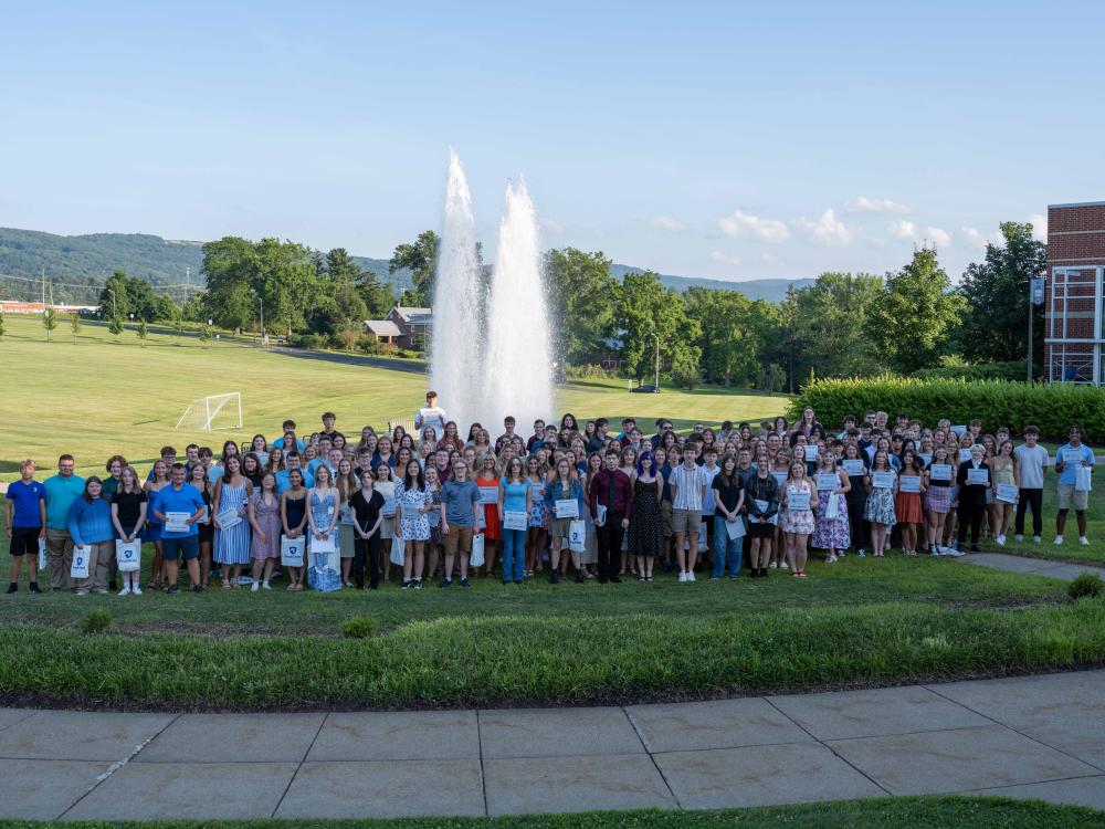 A large group of high school students stands in front of the fountain at Penn State Fayette, holding certificates and gift bags during the 15th annual 4.0 Club ceremony.